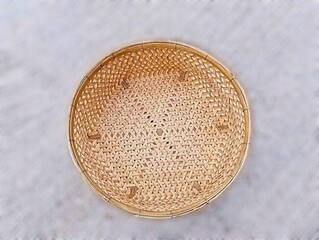 In the picture is a tray or wicker material made from brown bamboo in the shape of a circle with a thick edge. The inside is woven into various patterns that are reminiscent of ancient patterns and ha