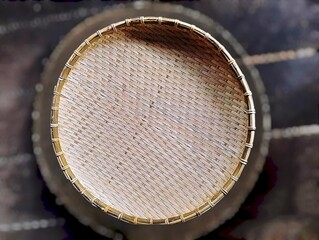 In the picture is a tray or wicker material made from brown bamboo in the shape of a circle with a thick edge. The inside is woven into various patterns that are reminiscent of ancient patterns and ha