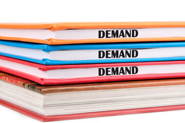 Concept word DEMAND on the ends of notebooks lying on top of each other on a white background