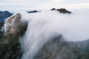 Aerial view of majestic mountain ridges at sunrise with falling fog from top of Pico do Areeiro, Madeira island, Portugal