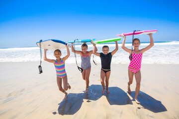 Group of young girls carrying their boogie boards at the beach after playing in the scenic Pacific Ocean. Fun summer lifestyle concept photo