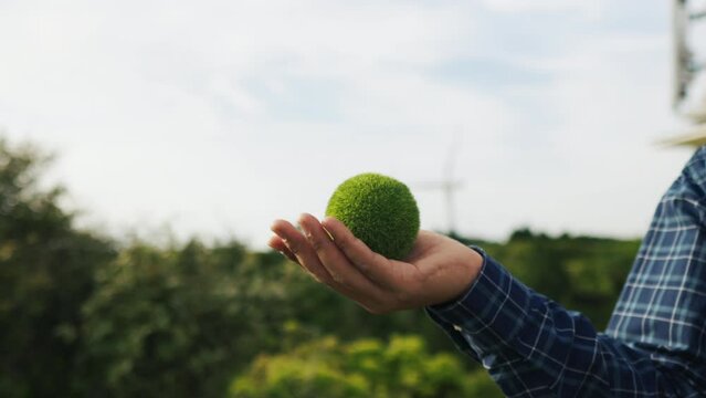 Hand holding a green earth ball to protect the earth on a tropical nature wind farm background. sustainable environmental concept esg, net zero