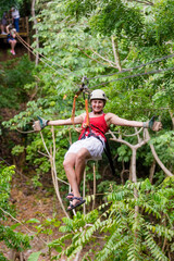 Smiling woman enjoying a jungle zip line adventure while on vacation in Costa Rica. Arms spread as she zips down a scenic mountain