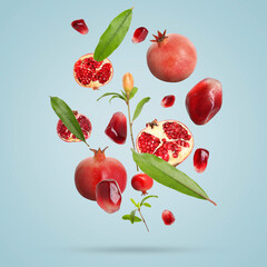 Fresh pomegranates, seeds and leaves in air on light blue background