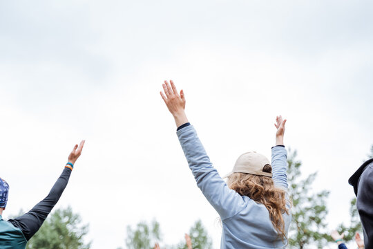 At a lively outdoor event, a diverse group of individuals joyfully come together, raising their arms in unity and celebrating in nature with enthusiasm and happiness