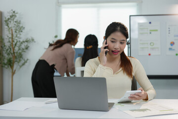 Young young woman with creative Asian business team, office colleagues using smartphone to contact business customers online Successful partnership in teamwork, startup business concept.