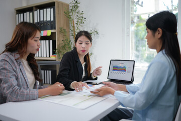 Young Asian female colleagues working together Analyze data on a laptop Discuss finding innovative business projects online to increase effective communication ideas, growth charts.