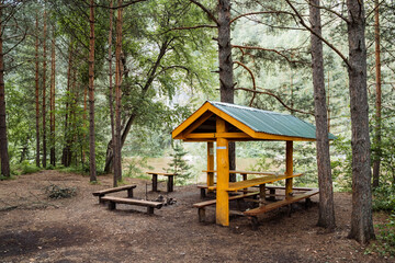 Amidst the forest stands a wooden picnic table with a green roof, offering a serene spot for leisure and relaxation within the natural landscape. The setting exudes tranquility and peace