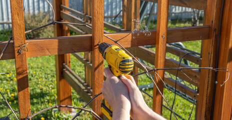 A man uses a cordless drill to assemble a wooden pergola, demonstrating home improvement and...