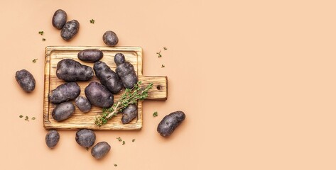 Wooden board with raw purple potatoes and thyme on orange background with space for text