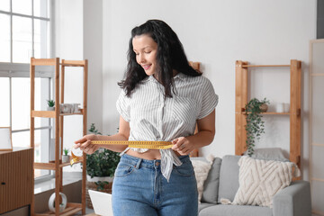 Beautiful young woman measuring her waist at home. Weight loss concept