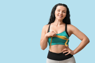 Obraz premium Beautiful young sporty woman measuring her breast on blue background. Weight loss concept