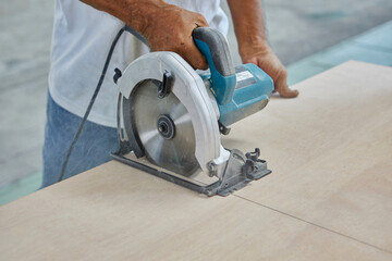 Midsection of man using circular saw cutting wooden board 
