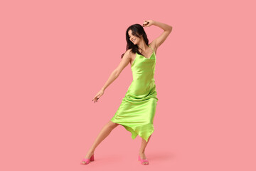 Beautiful young woman in stylish green dress dancing on pink background