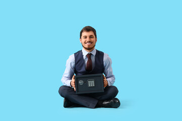 Happy young man with safe box sitting on blue background