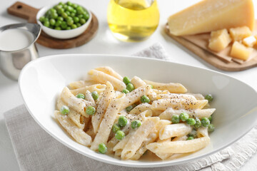 Delicious pasta with green peas and creamy sauce in bowl on white table