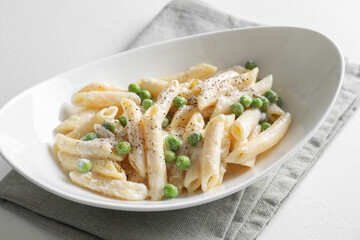 Delicious pasta with green peas and creamy sauce in bowl on white table