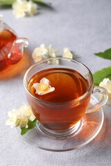 Hot jasmine tea in cup and flowers on light grey table