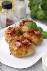 Delicious baked potatoes with bacon and basil on table, closeup