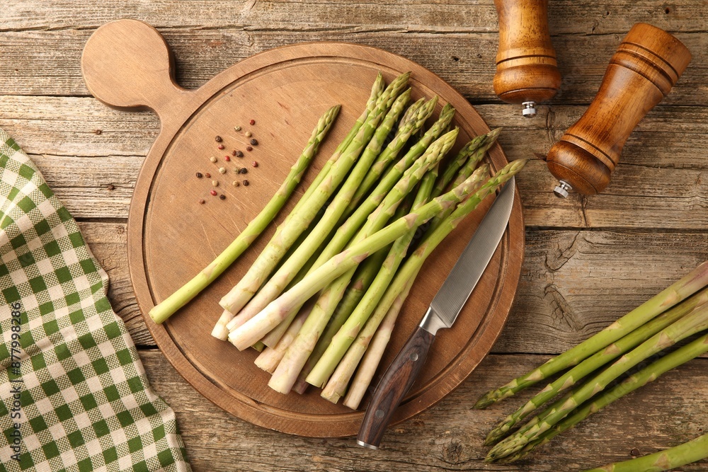 Wall mural board with fresh green asparagus stems, spices and knife on wooden table, flat lay