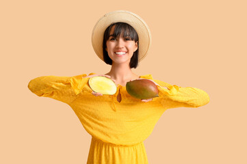 Beautiful young woman with ripe mangoes on beige background
