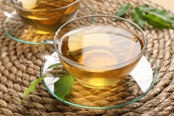 Refreshing green tea in cup and leaves on wicker mat, closeup