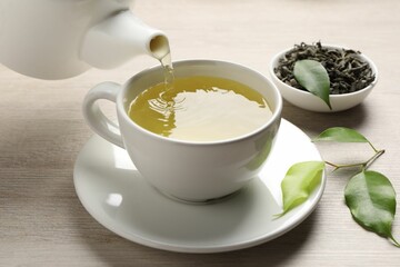 Pouring refreshing green tea into cup at wooden table, closeup