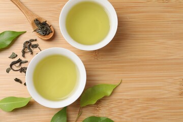 Refreshing green tea in cups, spoon and leaves on wooden table, flat lay. Space for text