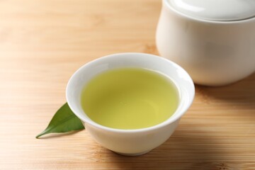 Refreshing green tea in cup, sugar bowl and leaf on wooden table, closeup