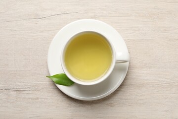 Refreshing green tea in cup and leaf on wooden table, top view
