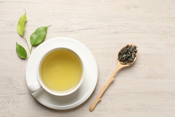 Refreshing green tea in cup, spoon and leaves on wooden table, flat lay