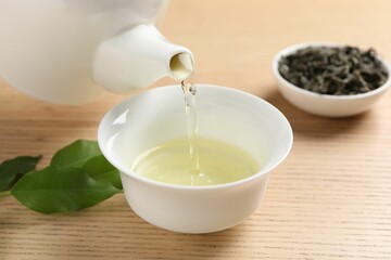 Pouring refreshing green tea into cup at wooden table, closeup