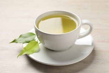 Refreshing green tea in cup and leaves on wooden table, closeup
