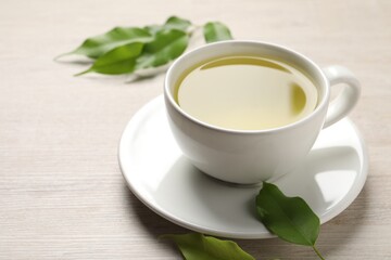 Refreshing green tea in cup and leaves on wooden table, closeup