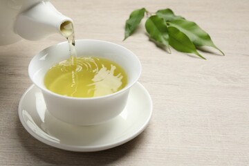 Pouring refreshing green tea into cup at wooden table, closeup. Space for text