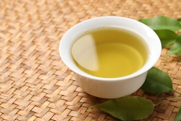 Refreshing green tea in cup and leaves on table, closeup