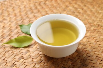 Refreshing green tea in cup and leaves on table, closeup