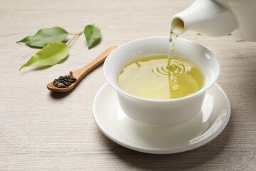 Pouring refreshing green tea into cup at wooden table, closeup
