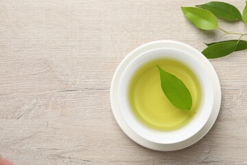 Refreshing green tea in cup and leaves on wooden table, flat lay. Space for text