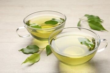 Refreshing green tea in cups and leaves on wooden table, closeup