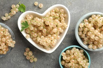 Fresh white currant berries in bowls and green leaves on gray textured table, flat lay
