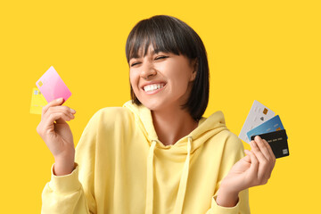 Beautiful young woman with many credit cards on yellow background