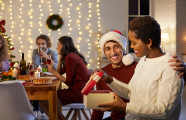 Smiling Caucasian man greeting excited African American woman with Christmas give presents. Happy multiracial friends exchange gifts on New Year eve. Winter holiday celebration concept.