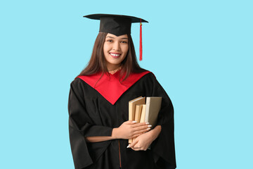 Young female graduate with books on blue background
