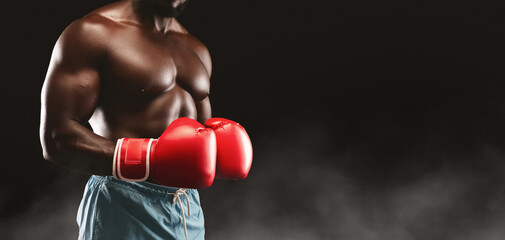 A shirtless boxer wearing red boxing gloves stands in a fighting stance against a black background...