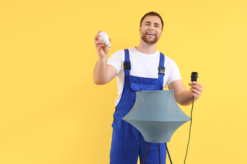 Male electrician changing light bulb in standard lamp on yellow background