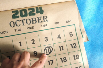 Hand pointing on October 10 2024 date on calendar flat lay in blue background.	World Mental Health...