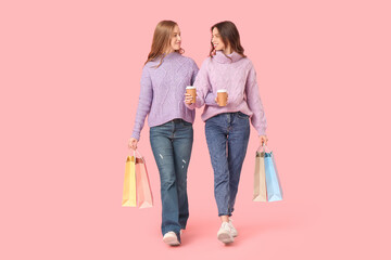 Young sisters with paper cups of coffee  and shopping bags on pink background