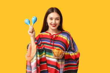 Portrait of young woman in colorful poncho with maracas and tortilla chips on yellow background. National Tortilla Chip Day celebration