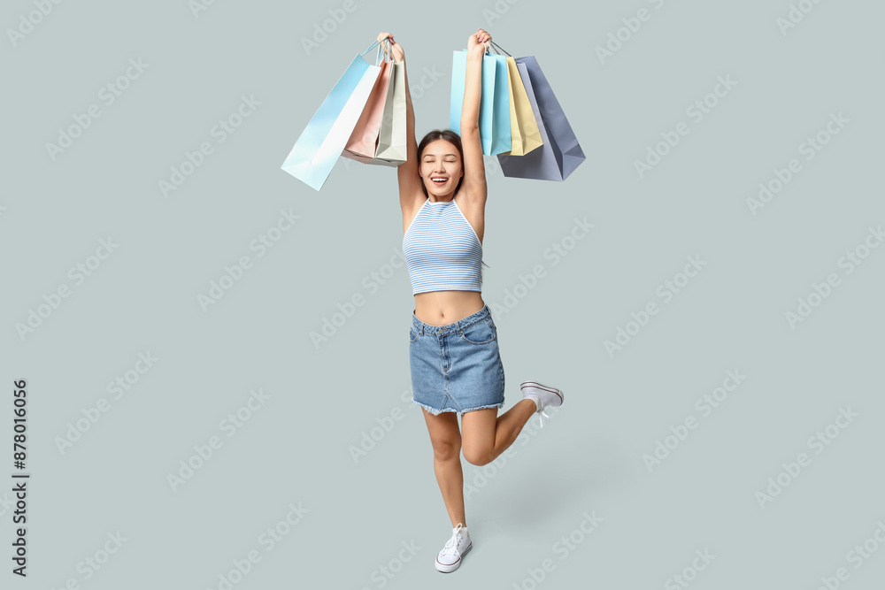 Wall mural Fashionable young Asian woman in stylish denim skirt with shopping bags on grey background